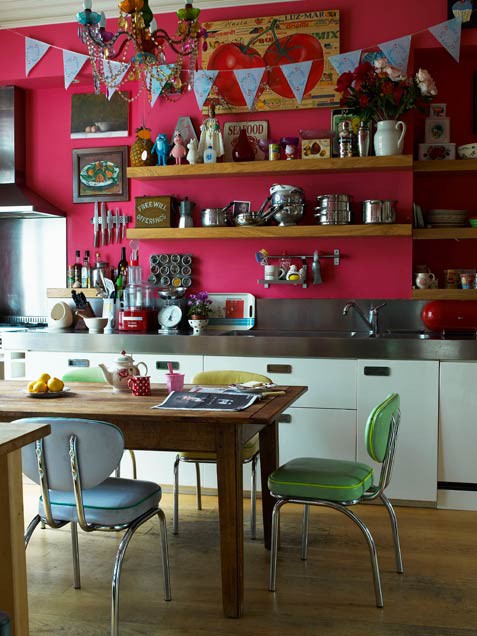 una cucina eclettica con pareti rosa caldo, elettrodomestici in acciaio inossidabile e alzatina, un tavolo in legno e sedie color pastello