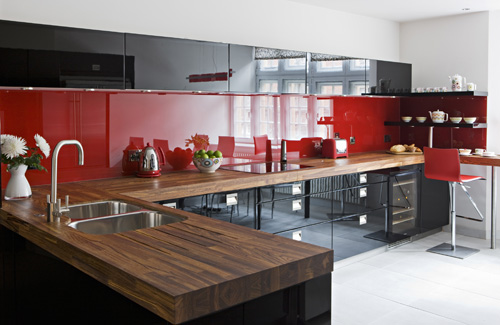 un'audace cucina contemporanea rossa e nera con un backsplash lucido e controsoffitti macellaio più elettrodomestici in acciaio inossidabile è molto audace e alla moda