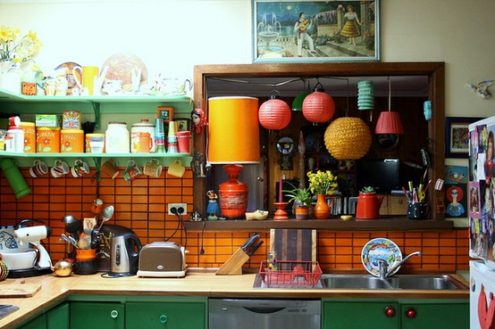 una cucina audace con armadi verdi, un alzatina in piastrelle arancioni, una mensola in legno e alcuni tocchi arancioni è molto divertente e stravagante