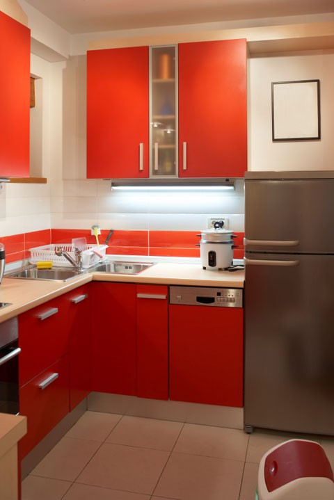 una cucina luminosa con mobili rossi e un backsplash in piastrelle audaci, piastrelle neutre e un frigorifero in acciaio inossidabile