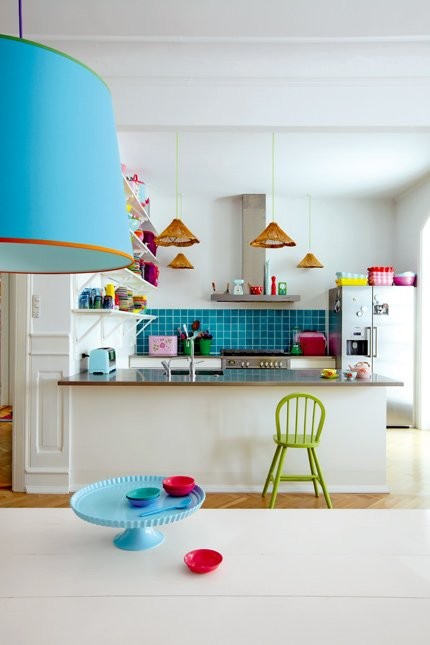 una cucina giocosa con mobili bianchi, elettrodomestici in acciaio inossidabile, un audace alzatina blu e lampade e alcuni tocchi colorati è divertente