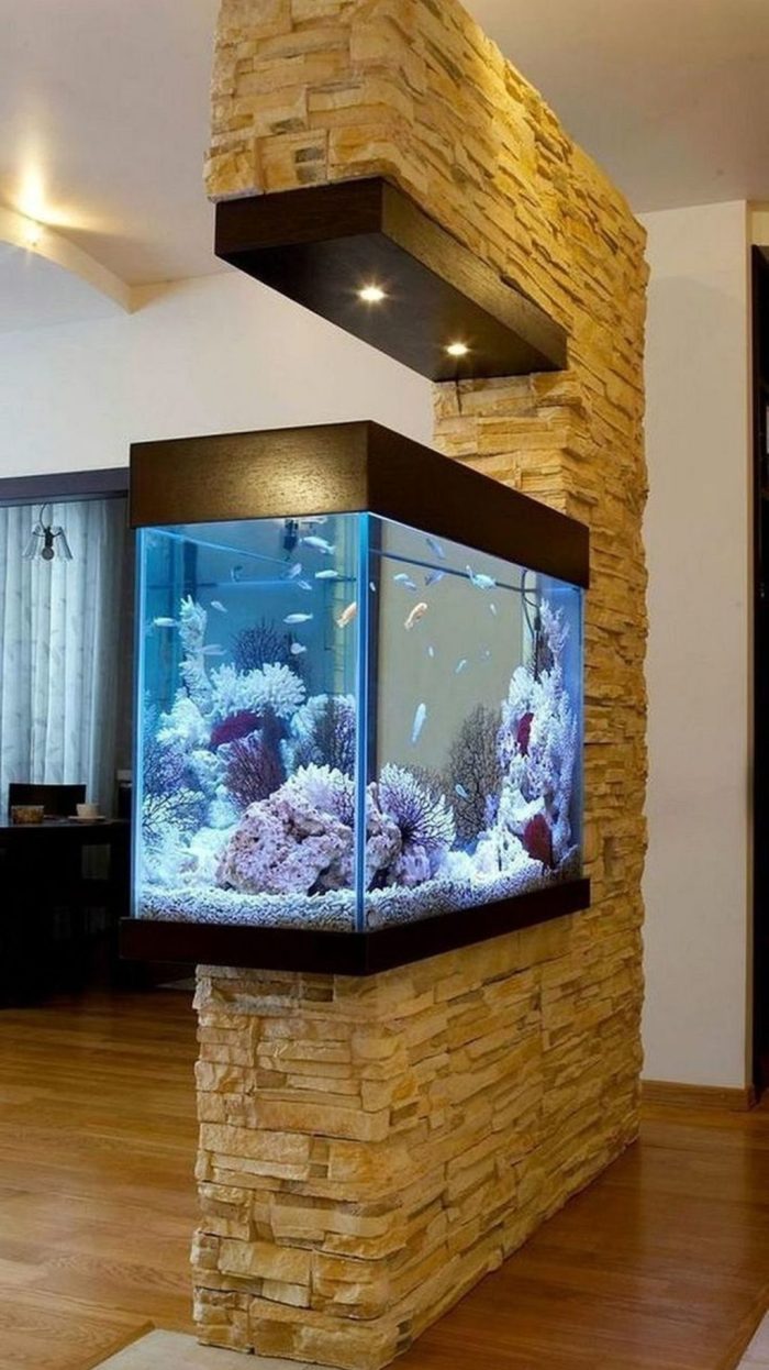 un muro di finta pietra con un acquario integrato e luci è un divisorio di spazio moderno e audace da scegliere
