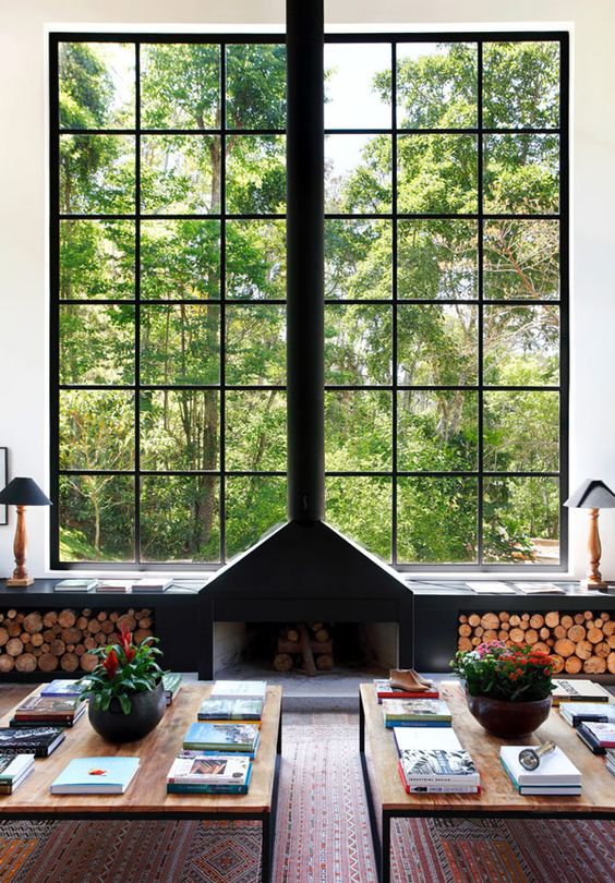un camino aperto vicino alla finestra e una panca davanzale con ripostiglio aperto per la legna da ardere si abbinano perfettamente a questo interno moderno