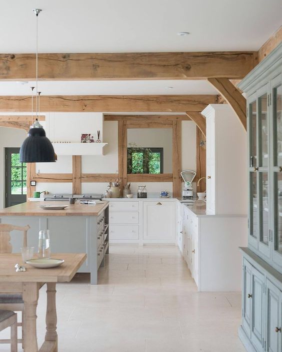 una cucina contemporanea con mobili bianchi, un'isola della cucina grigia e dettagli in legno più travi in ​​legno è molto accogliente