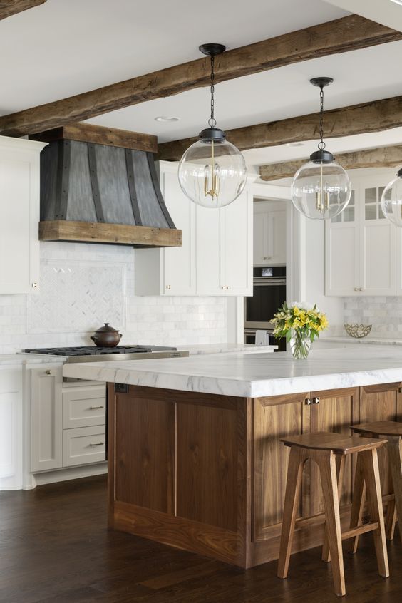 una cucina rustica in colori neutri, con isola cucina in legno e sgabelli e travi in ​​legno che rallegrano lo spazio