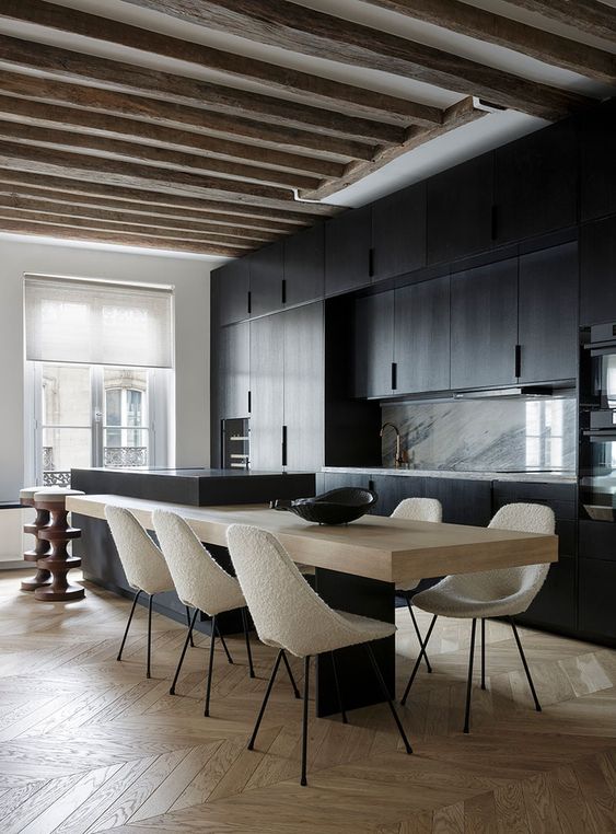 una cucina minimalista con ante nere, alzatina in marmo, isola cucina in due parti e travi in ​​legno grezzo