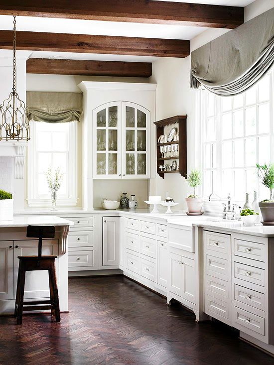 una cucina bianca vintage con mobili eleganti, travi in ​​legno scuro e sottotetti che aggiungono interesse, tende grigie e verdi