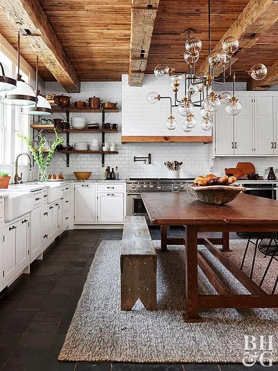 una cucina raffinata e chic in bianco, con mobili eleganti, tavolo e panche in legno, soffitto in legno con travi a vista ed eleganti lampadari