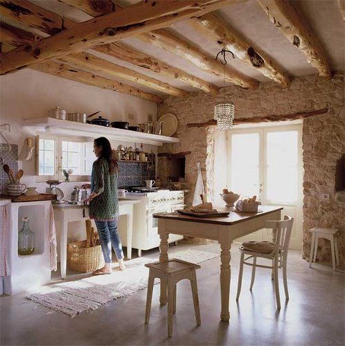 una cucina colonica francese con pareti in pietra, travi in ​​legno a vista e mobili vintage bianchi e un lampadario di cristallo