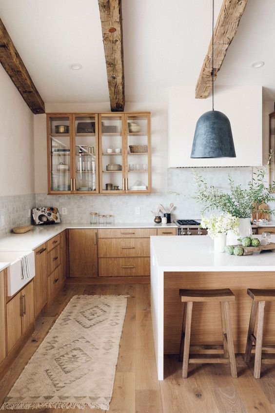 un'accogliente cucina colonica moderna con pensili dai colori chiari, travi in ​​legno e sgabelli che riscaldano lo spazio