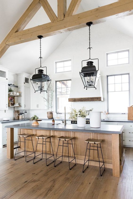 una cucina bianca ariosa e chic con un'isola cucina in legno e travi in ​​legno sul soffitto oltre a raffinate lampade vintage