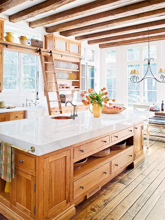 una cucina colonica dai colori caldi con mobili dai colori intensi, ripiani in marmo bianco, travi in ​​legno sul soffitto e un lampadario vintage
