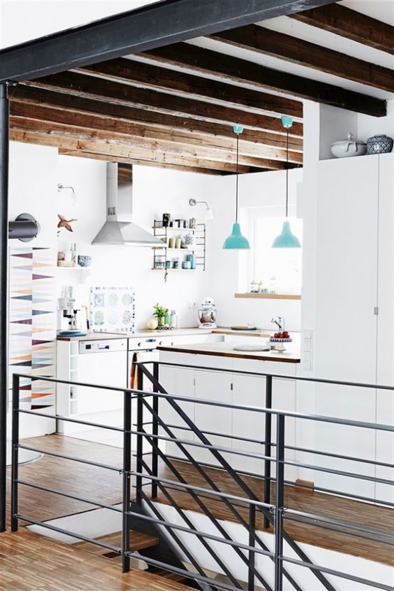 una cucina bianca minimalista con mobili eleganti, ripiani in legno, travi in ​​legno per un tocco caldo e lampade a sospensione blu sembra fresca e chic