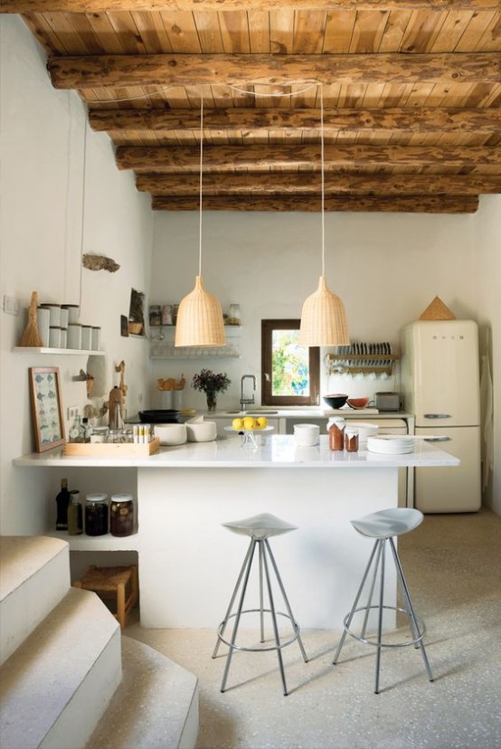 una moderna cucina bianca con un'isola cucina bianca di grandi dimensioni, un soffitto in legno con travi a vista per un'atmosfera calda e accogliente e lampade a sospensione intrecciate