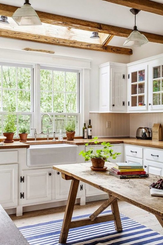Una cucina rustica bianca con ripiani in legno, un'isola da cucina con tavolo in legno e travi in ​​legno che rendono accogliente la cucina