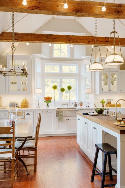 una moderna cucina colonica bianca con mobili chic, travi in ​​legno con luci ed eleganti lampadari e lampade