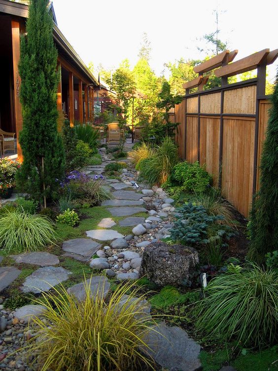 un giardino di ispirazione giapponese con piastrelle di roccia, ciottoli, ceppi d'albero, vegetazione, erbe e un albero alto per un look zen