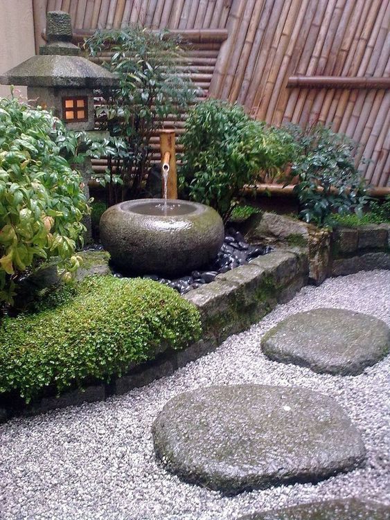 ciottoli, rocce, erba, arbusti, una fontana con ciotola di pietra e una lanterna di pietra per un cortile giapponese incantevole e chic