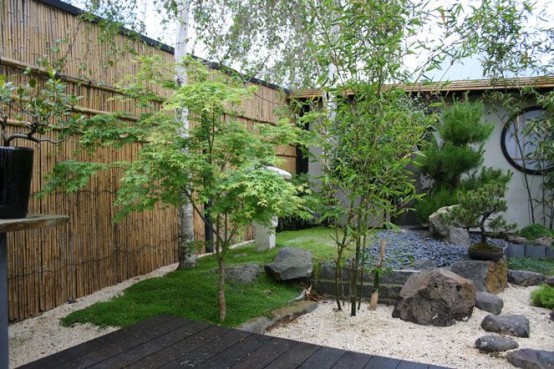 ciottoli bianchi, rocce, erba e alberi sottili più un muro di bambù per un giardino giapponese o un cortile