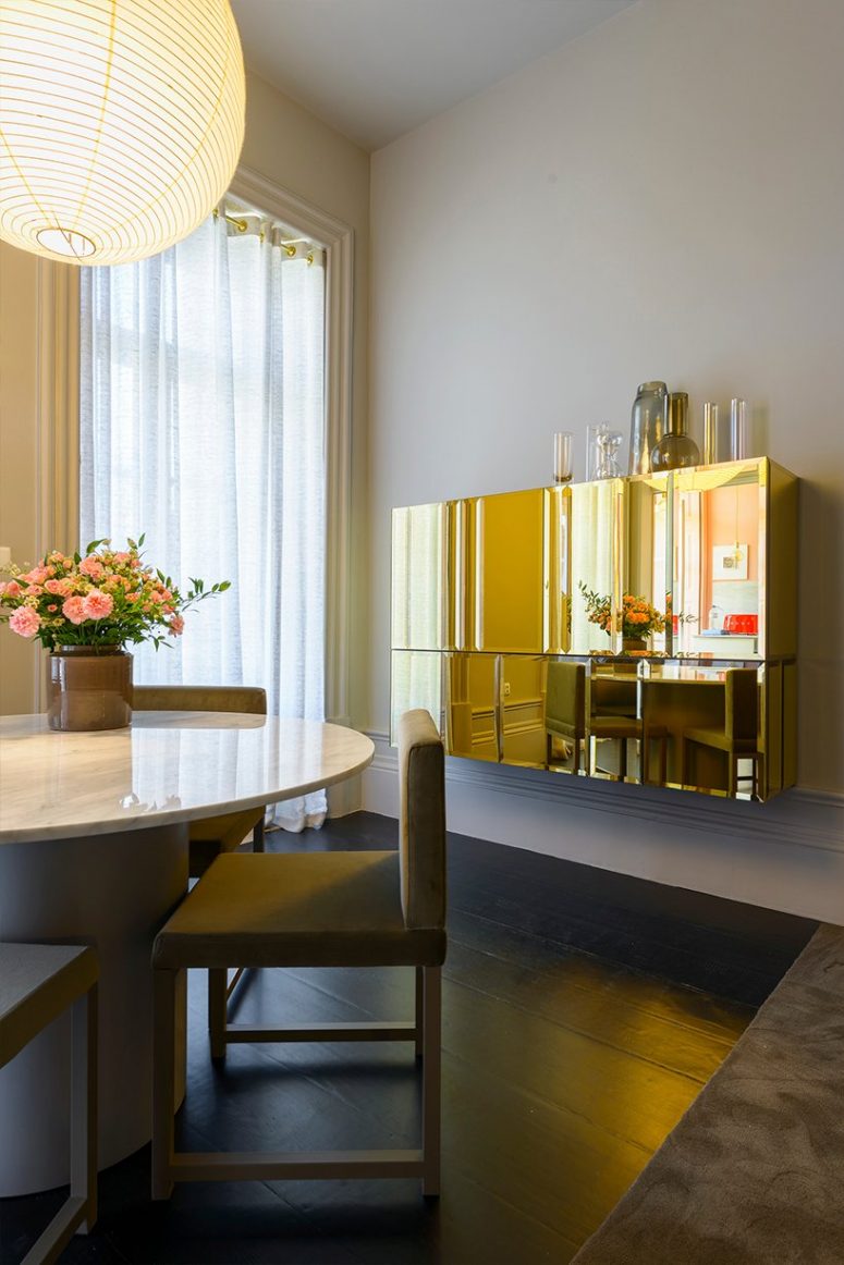 La sala da pranzo è molto raffinata, con un tavolo rotondo con un piano in marmo, sedie chic e uno splendido mobile in oro lucido sul muro