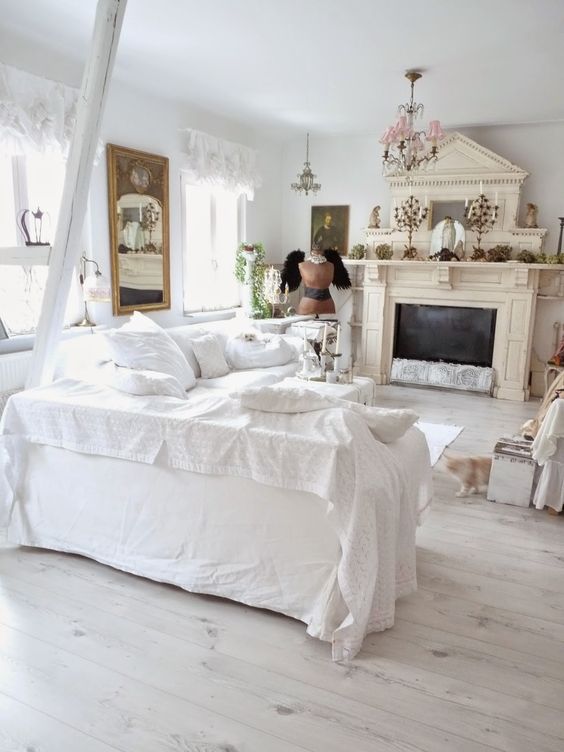 un accattivante soggiorno shabby chic in bianco, con un caminetto marrone chiaro, lampadari vintage, uno specchio e tende di pizzo