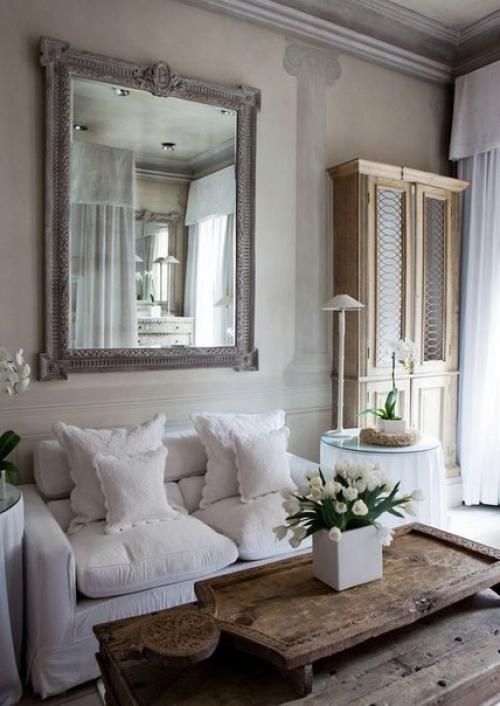 un soggiorno shabby chic neutro con un divano bianco, un grande specchio, un tavolo in legno grezzo e un grande armadio vintage