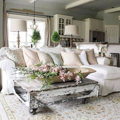 un soggiorno shabby chic neutro con un componibile bianco, un tavolo basso shabby, verde e fiori è accogliente