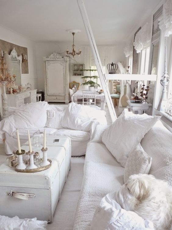 un soggiorno shabby chic bianco con mobili chic, una cassapanca bianca, cuscini bianchi e candele è molto elegante