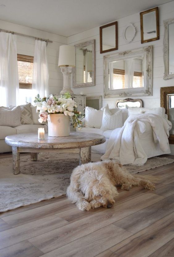 un soggiorno shabby chic bianco con una galleria di specchi, mobili bianchi, un tavolo squallido, lampade e fiori