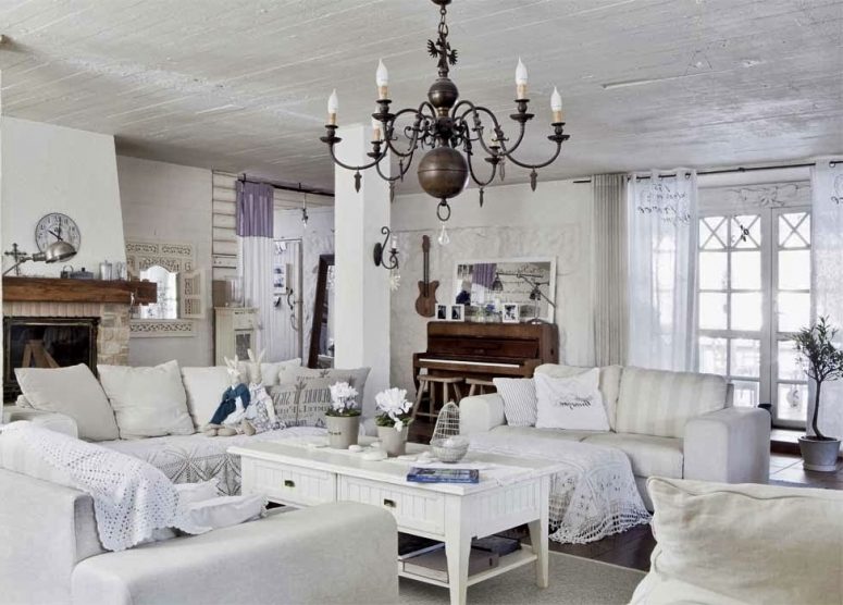 un soggiorno shabby chic bianco con mobili eleganti, un lampadario vintage, un tavolino basso, un camino in pietra e uncinetto e centrini