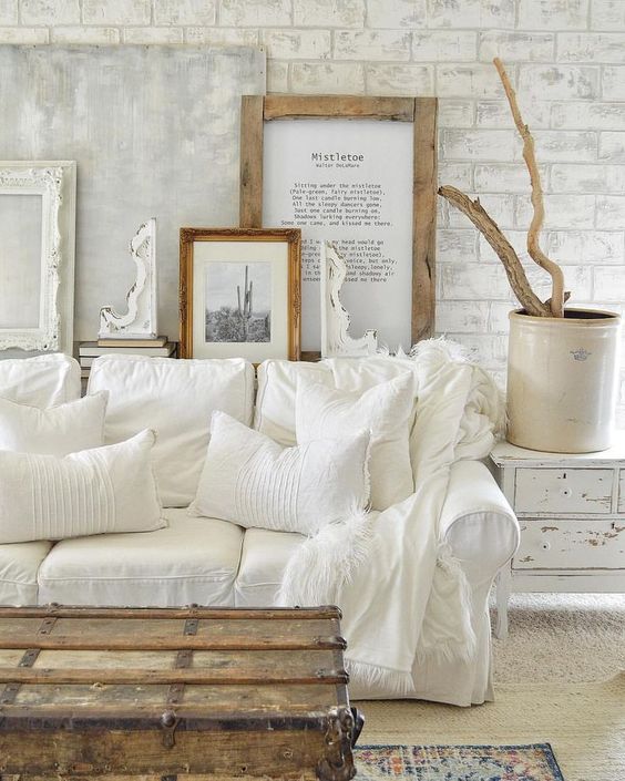 uno spazio living bianco shabby chic con una galleria a muro, un divano bianco, una credenza shabby e una cassapanca in legno