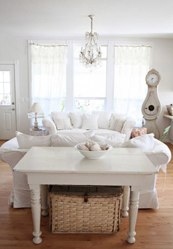 un soggiorno shabby chic bianco con mobili chic, tessuti neutri, un lampadario di cristallo e accessori e decorazioni vintage