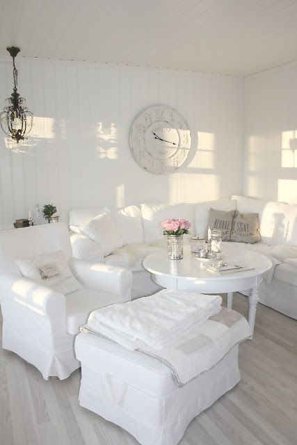 un soggiorno shabby chic bianco con mobili raffinati, un tavolo bianco, un orologio e un lampadario di cristallo è molto elegante