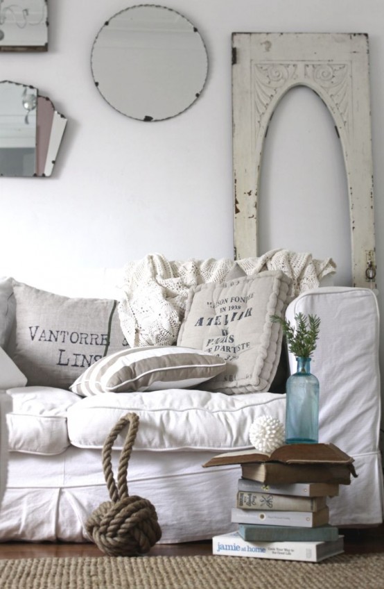 un soggiorno shabby chic bianco con mobili alla moda, una galleria a parete con specchi, un tappeto di iuta, alcune fioriture in un vaso è bellissimo