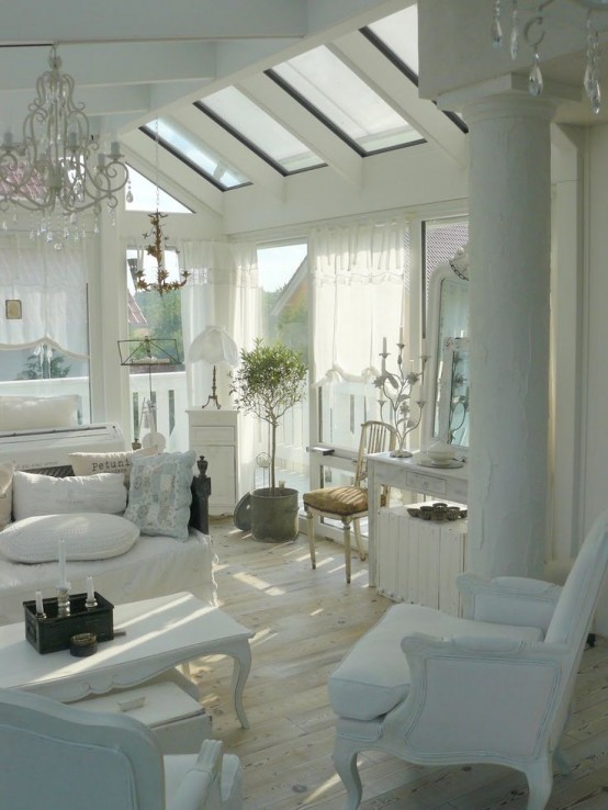 un soggiorno shabby chic bianco con lucernari, eleganti mobili bianchi, un lampadario di cristallo, una pianta in vaso e vegetazione