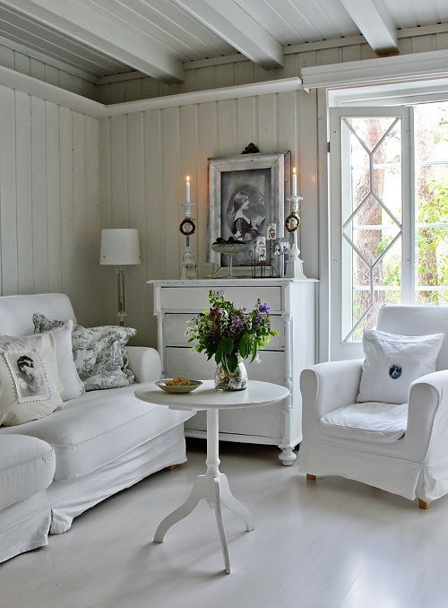 un soggiorno shabby chic neutro con mobili eleganti e chic, una credenza bianca, candele e piante in vaso è molto elegante