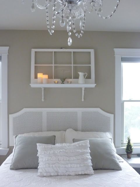 una mensola sopra il letto fatta di una mensola e una vecchia finestra, alcune candele, una brocca e altro arredamento per una camera da letto bianca vintage