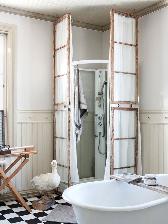 un bagno vintage con uno spazio doccia moderno ma rivestito con vecchi infissi e con stoffa bianca appesa