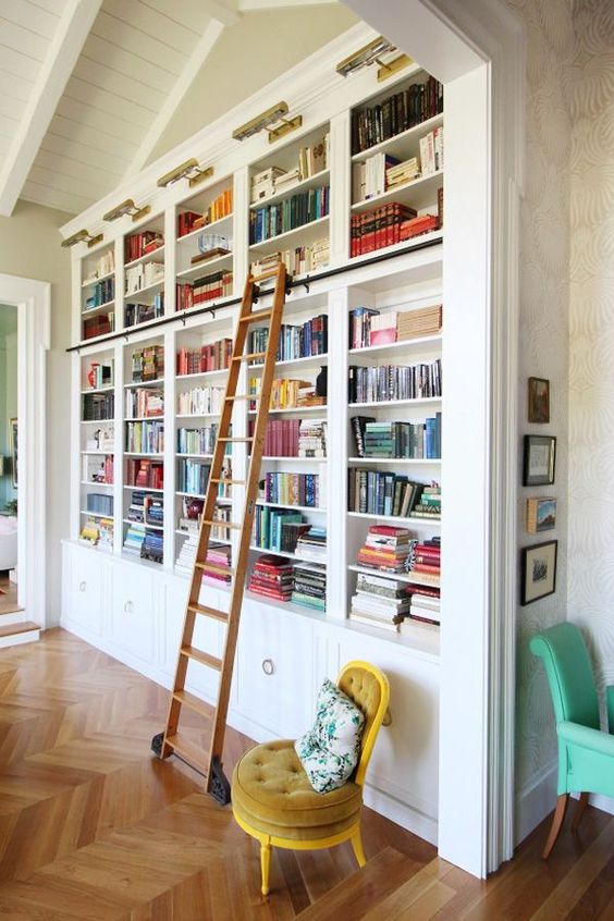 un'elegante librerie incassate con una scala, una sedia color senape e luci aggiuntive è molto chic