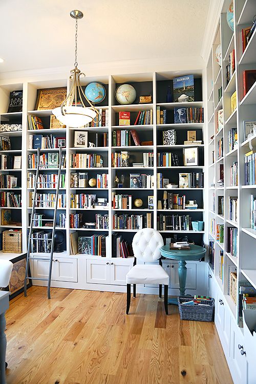 un elegante home office e una biblioteca in uno con scaffali integrati, una sedia bianca, una lampada a sospensione e alcuni oggetti vintage