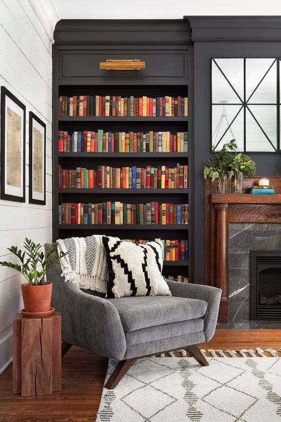 uno spazio elegante e lunatico con librerie scure incorporate, un camino in marmo e una sedia grigia per il massimo comfort