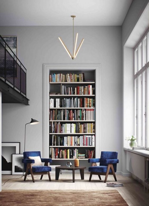 un elegante angolo di conversazione e lettura con sedie in velluto blu scuro, una grande libreria incorporata e un bellissimo lampadario