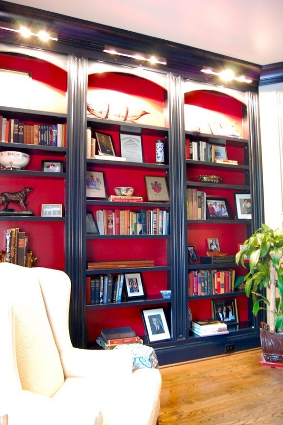 le eleganti librerie incorporate blu scuro con supporto rosso e luci aggiuntive sugli scaffali sono sorprendenti per uno spazio raffinato