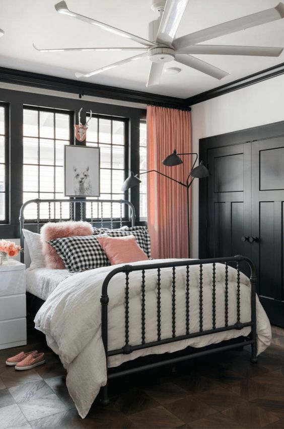 una graziosa camera da letto rosa, nera e bianca con pannelli neri, un letto forgiato, tende e cuscini rosa per un look chic