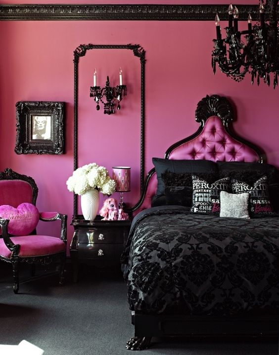 una drammatica camera da letto nera e rosa con pareti rosa brillante, una sedia, un letto rosa, un lampadario nero, biancheria da letto e cornici