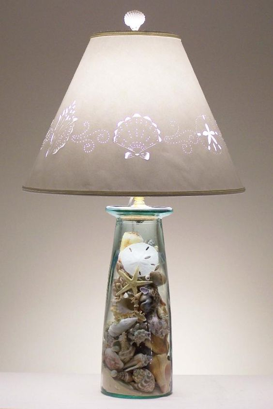 una bella lampada da tavolo con una base in vetro con conchiglie, stelle marine e sabbia da spiaggia all'interno e un paralume stampato per uno spazio da spiaggia