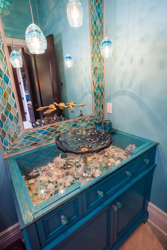 una vanità blu elettrico con un tavolo di vetro e conchiglie e ciottoli sotto di esso più lampade a sospensione ispirate alle meduse