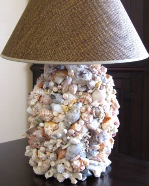 una lampada da tavolo ispirata al mare con una base ricoperta di conchiglie di vari colori e dimensioni e un paralume di juta per una casa rustica al mare