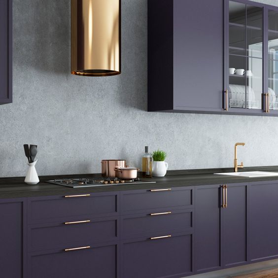 una cucina viola scuro con alzatina in pietra grigia, ripiani in pietra nera e tocchi d'oro qua e là