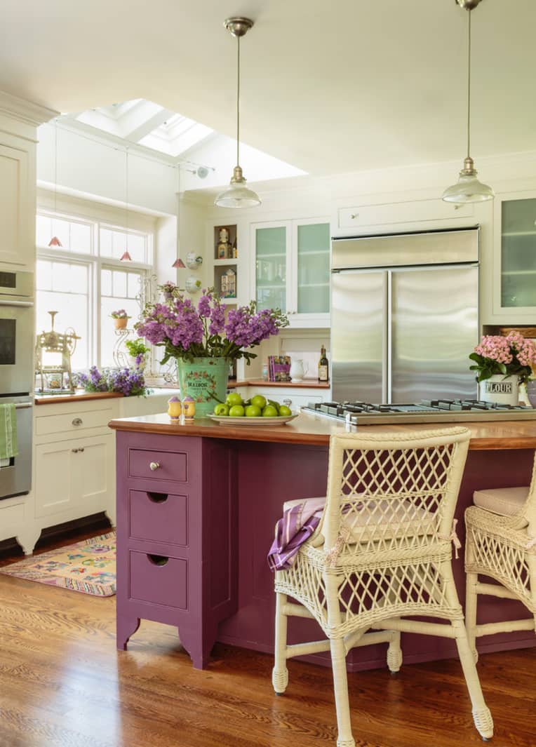 una cucina rustica vintage neutra con un'isola da cucina viola, lucernari e lampade a sospensione e alcune fioriture viola